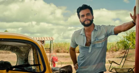 Wagner Moura em cena de O Agente Secreto ao lado de carro amarelo em área rural.