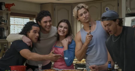 Elenco de Off Campus reunido em uma cozinha, com Hannah ao centro e jogadores da Briar University ao redor durante cena descontraída