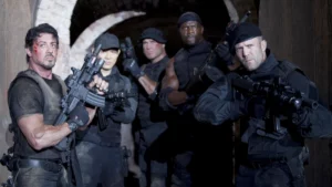 Integrantes de Os Mercenários armados em missão dentro de um túnel escuro, em cena clássica de ação da franquia.