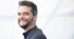 Wagner Moura sorri usando terno escuro durante aparição pública em evento.