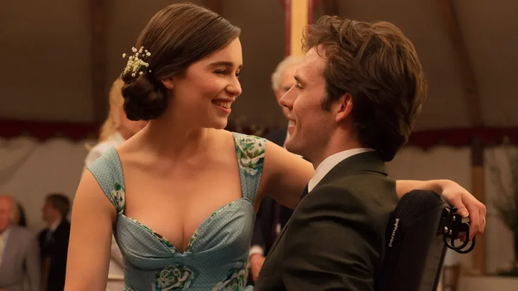 Uma fotografia de Emilia Clarke e Sam Claflin como Louisa Clark e Will Traynor do filme Como Eu Era Antes de Você. Eles estão olhando um para o outro, sorrindo e sentados à mesa de jantar. Louisa está usando um vestido com estampa azul e verde com pequenas flores brancas no cabelo, que está preso em um coque. Will está sentado em uma cadeira de rodas usando um terno verde. Outras pessoas são visíveis ao fundo, fora de foco.