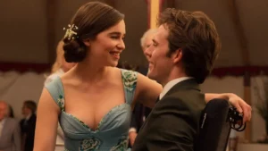 Uma fotografia de Emilia Clarke e Sam Claflin como Louisa Clark e Will Traynor do filme Como Eu Era Antes de Você. Eles estão olhando um para o outro, sorrindo e sentados à mesa de jantar. Louisa está usando um vestido com estampa azul e verde com pequenas flores brancas no cabelo, que está preso em um coque. Will está sentado em uma cadeira de rodas usando um terno verde. Outras pessoas são visíveis ao fundo, fora de foco.