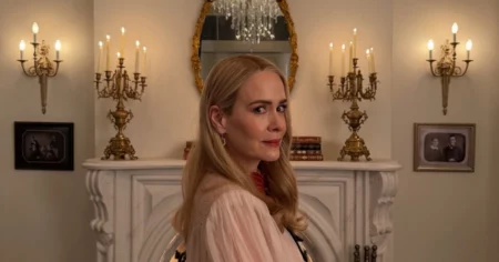 Atriz de American Horror Story 13 posa diante de lareira em ambiente iluminado por candelabros