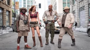 Dwayne Johnson, Karen Gillan, Kevin Hart e Jack Black aparecem caracterizados como seus personagens de Jumanji: Mundo Aberto em uma rua cercada por prédios.