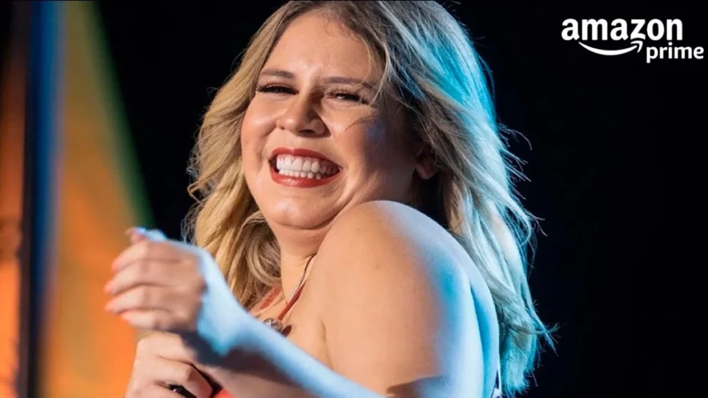 Marília Mendonça sorrindo no palco durante apresentação, com microfone na mão, sob luzes de show e fundo escuro.