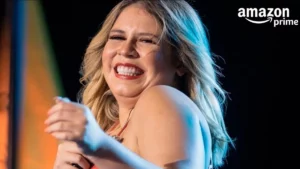 Marília Mendonça sorrindo no palco durante apresentação, com microfone na mão, sob luzes de show e fundo escuro.