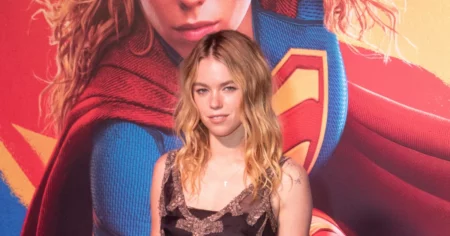 Milly Alcock posa em evento de Supergirl diante de painel do filme da DC após divulgação do cachê da atriz