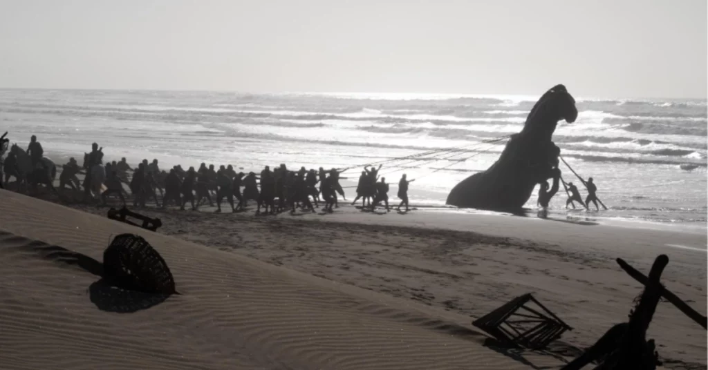 A Odisseia pode superar Oppenheimer na estreia; entenda Equipe puxa uma réplica do Cavalo de Troia pela praia durante as filmagens de A Odisseia