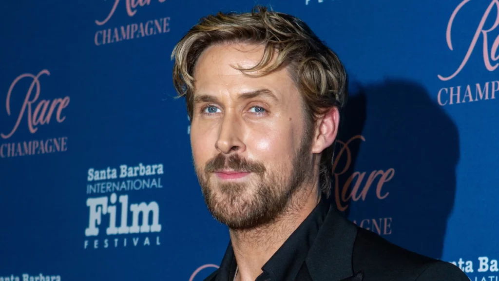 Ryan Gosling posa em evento com fundo azul.