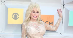Dolly Parton no cinema: relembre 9 filmes da cantora e atriz Dolly Parton posa sorridente em evento, usando vestido claro com detalhes bordados