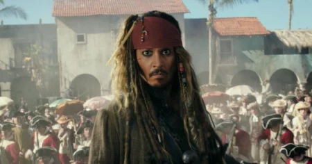 Johnny Depp caracterizado como Jack Sparrow, com faixa vermelha na cabeça, cabelos longos com tranças e figurino de pirata, diante de uma multidão em cena de Piratas do Caribe