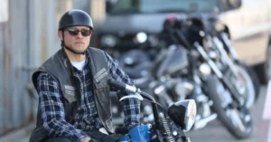 Charlie Hunnam aparece de capacete, óculos escuros e colete de motociclista sentado sobre uma moto em cena de Sons of Anarchy