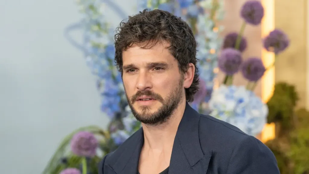 Kit Harington aparece em close, com barba e cabelos escuros, durante um evento.