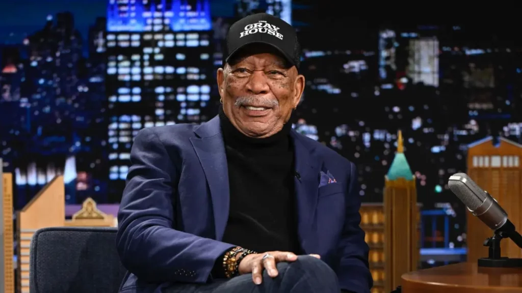 Morgan Freeman revela arrependimento na carreira e o único astro que inveja Morgan Freeman sentado em um estúdio de televisão, usando terno azul-marinho, blusa preta e boné preto.